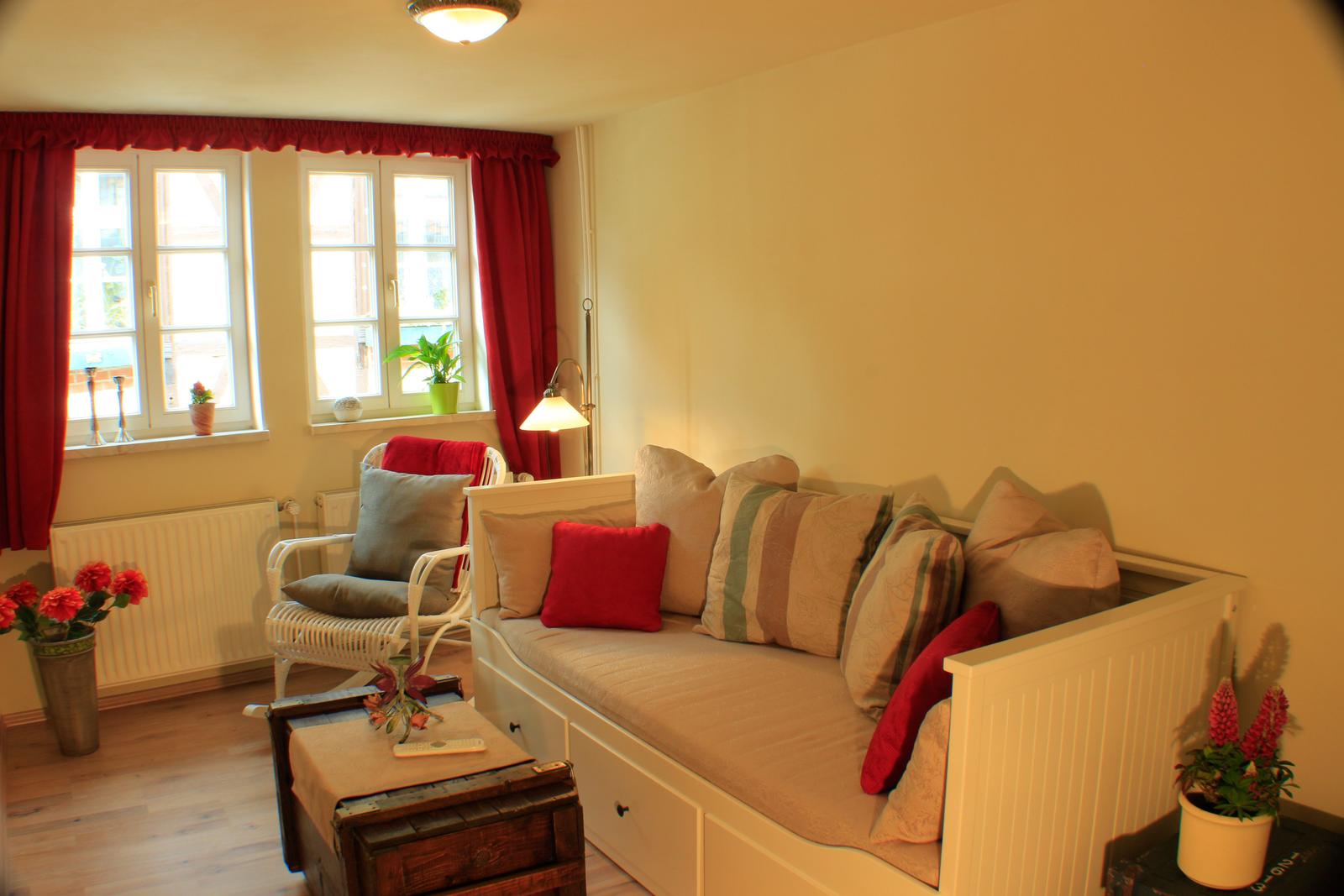 Ein Wohnzimmer mit Sofa, Sessel, Fenstern und Pflanzen.
