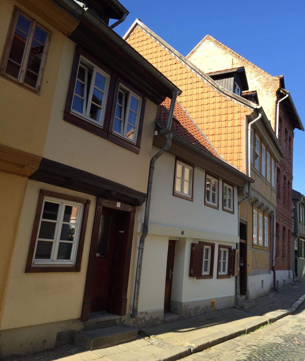 Straße mit historischen Häusern und roten Ziegeldächern unter blauem Himmel.