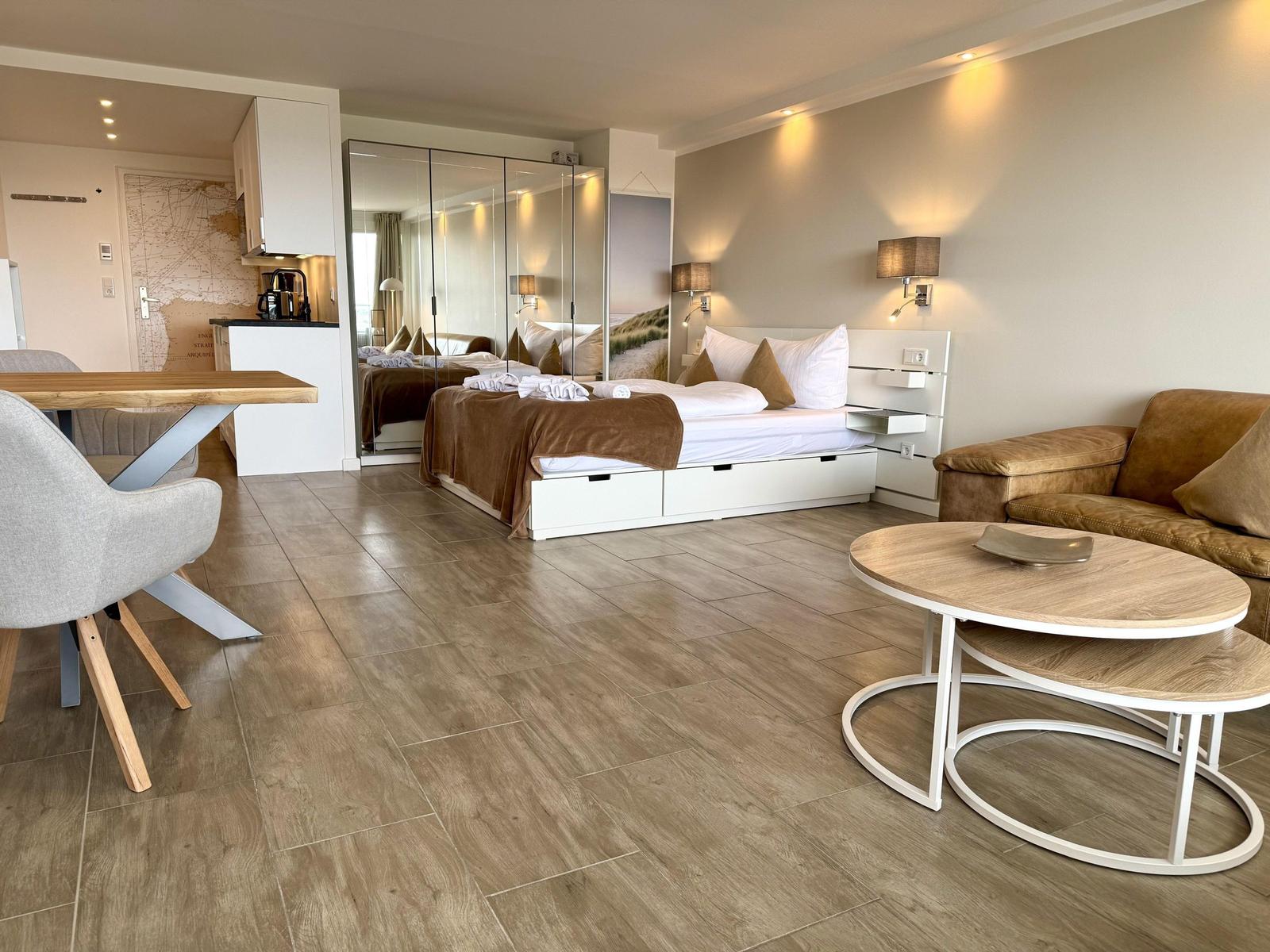 Ein Schlafzimmer mit Bett, Sofa und Küchenbereich. Holzboden und Spiegelschrank.