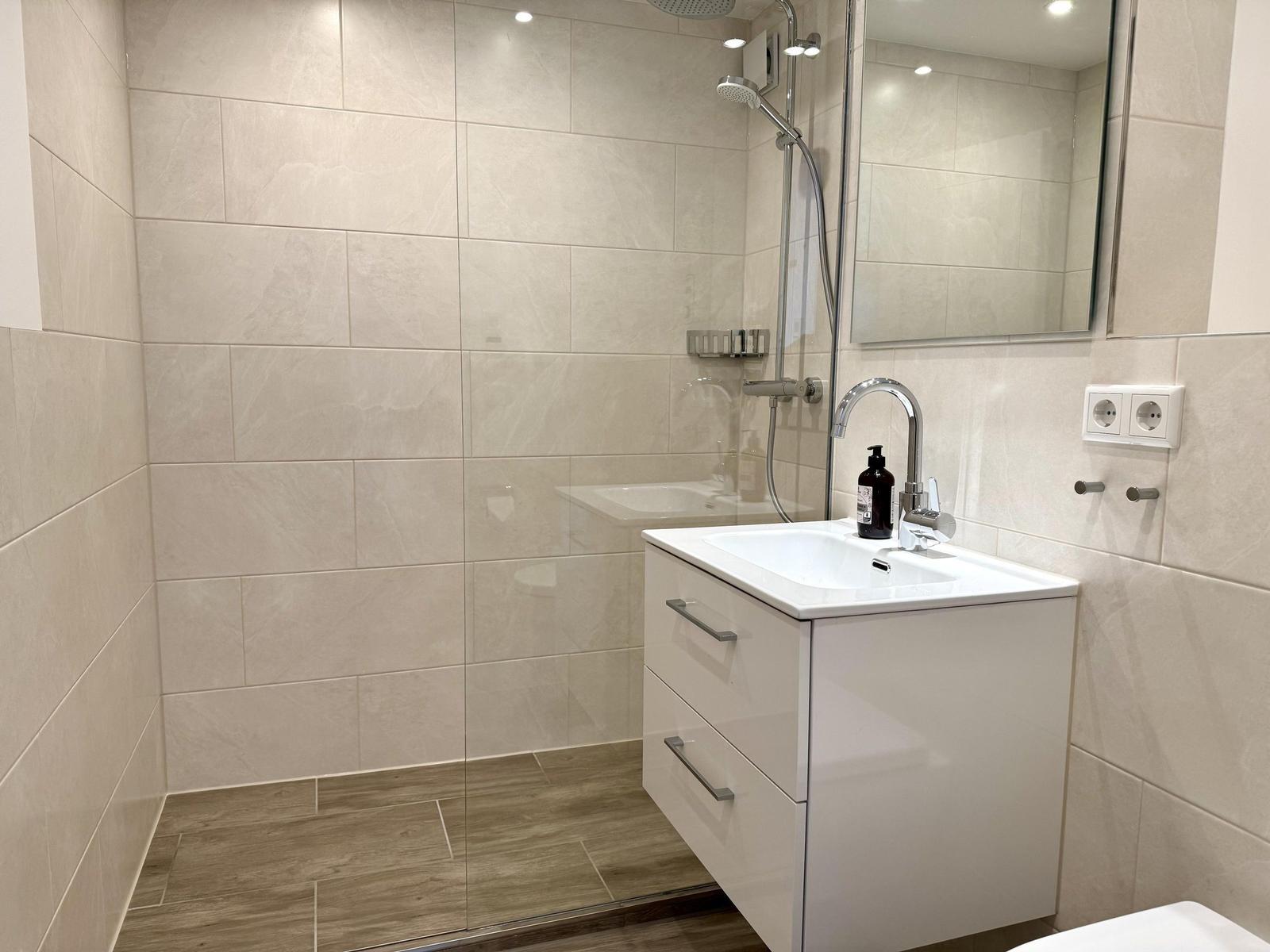 Badezimmer mit Dusche, Waschbecken und Spiegel. Fliesenwand und Holzboden.