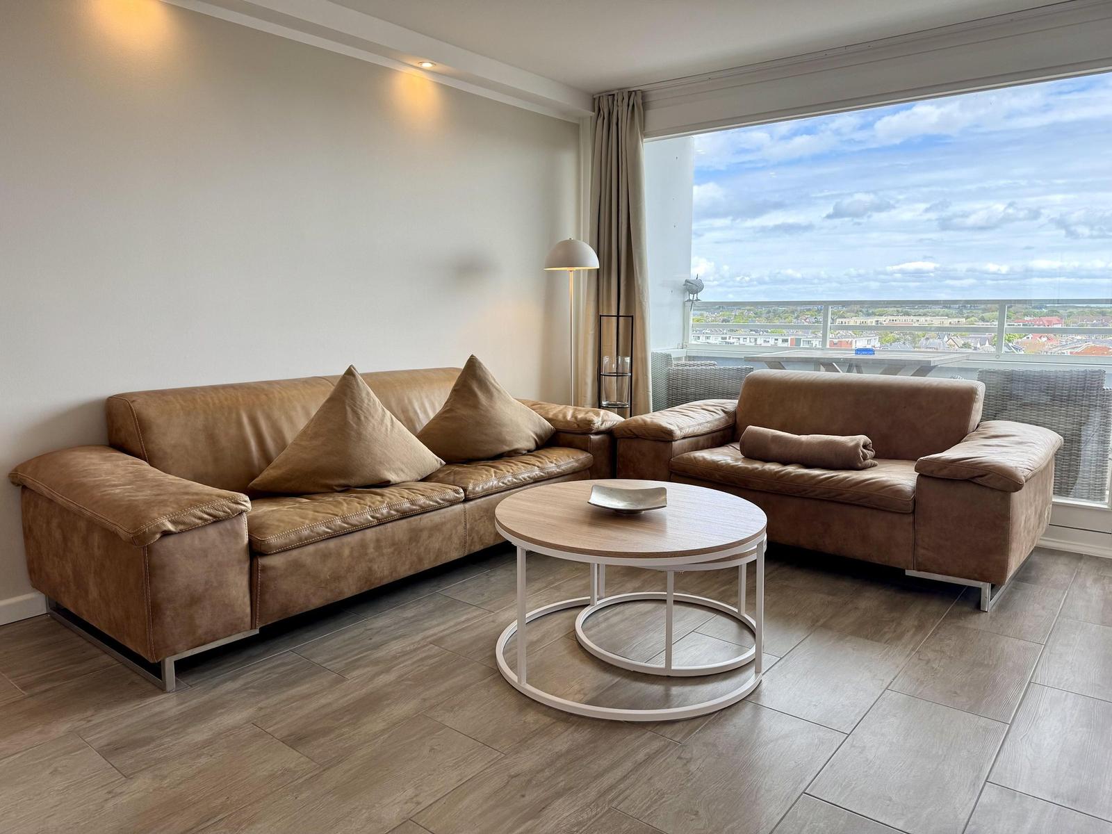Wohnzimmer mit braunen Sofas, runden Tisch und Blick auf Balkon.