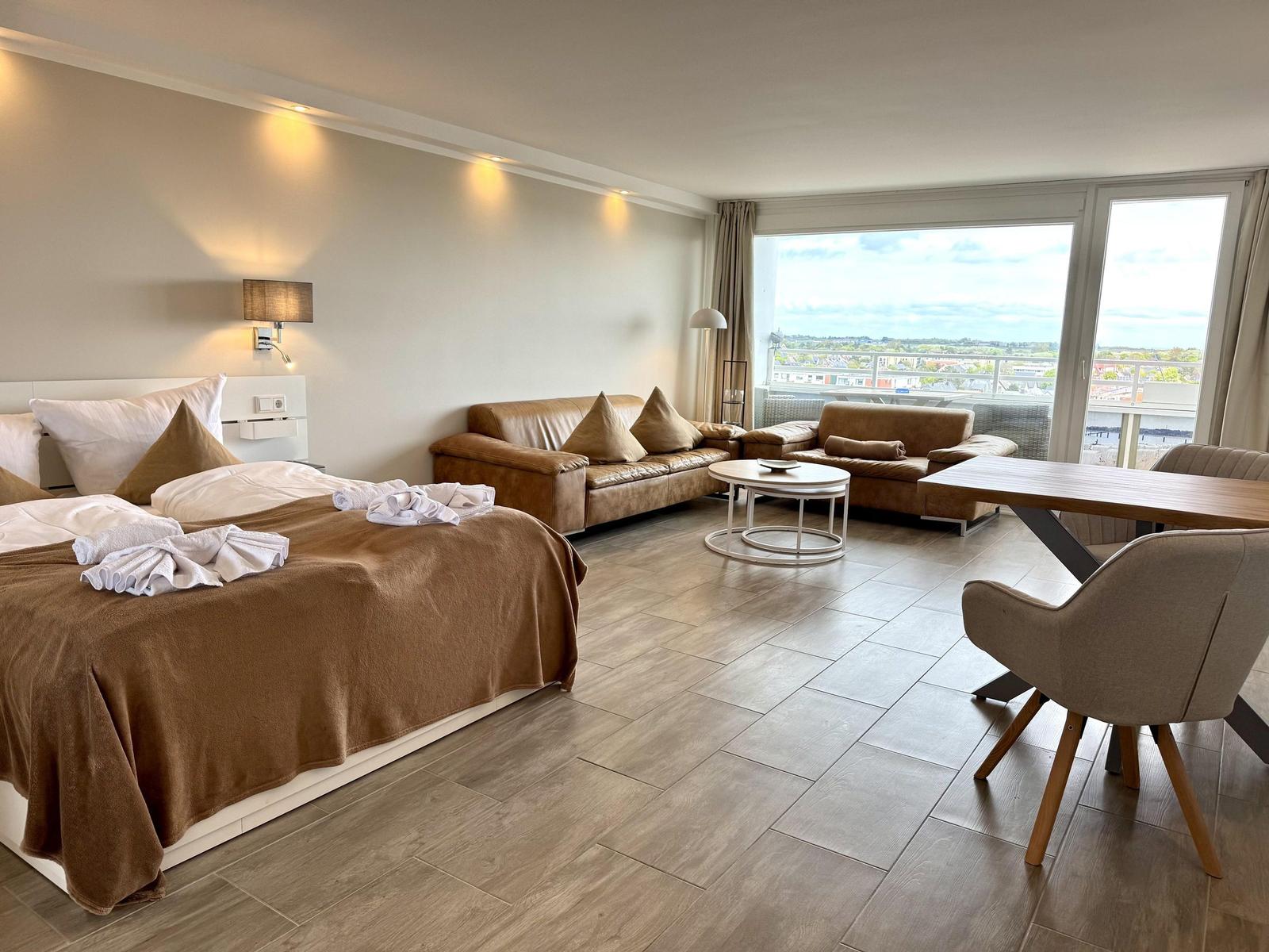 Ein Schlafzimmer mit Bett, Sofa, Tisch und Balkon mit Aussicht.