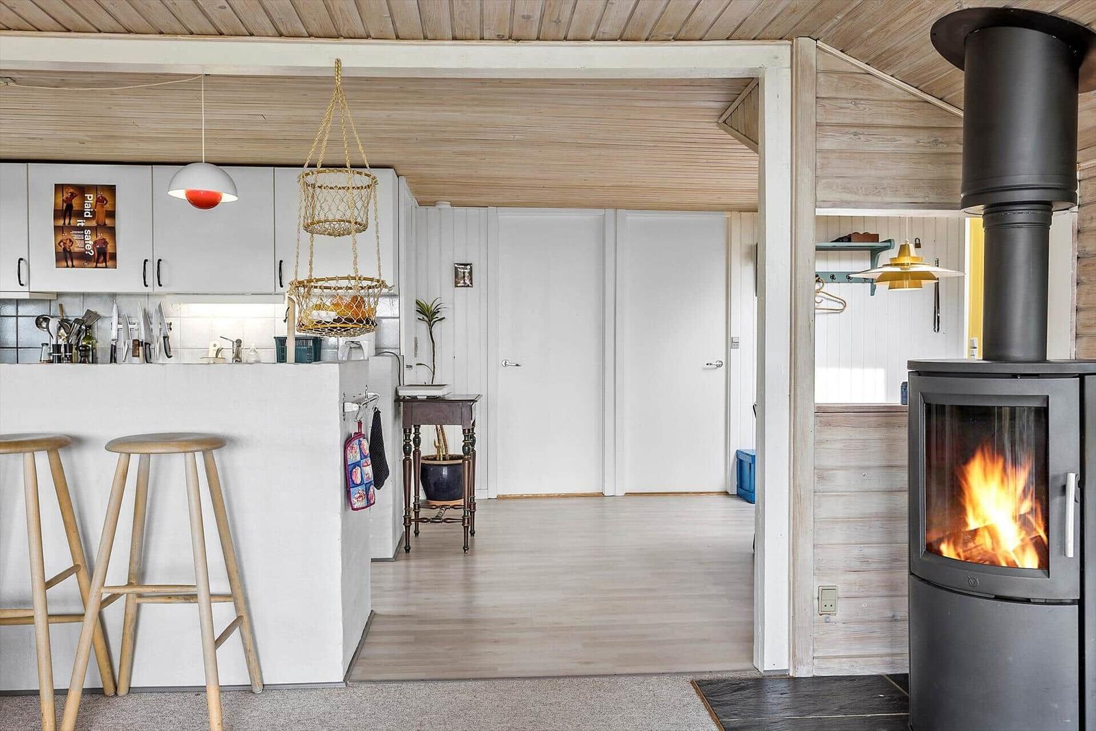 Küche mit Holzdecke, Kaminofen und Sitzgelegenheiten im Vordergrund.