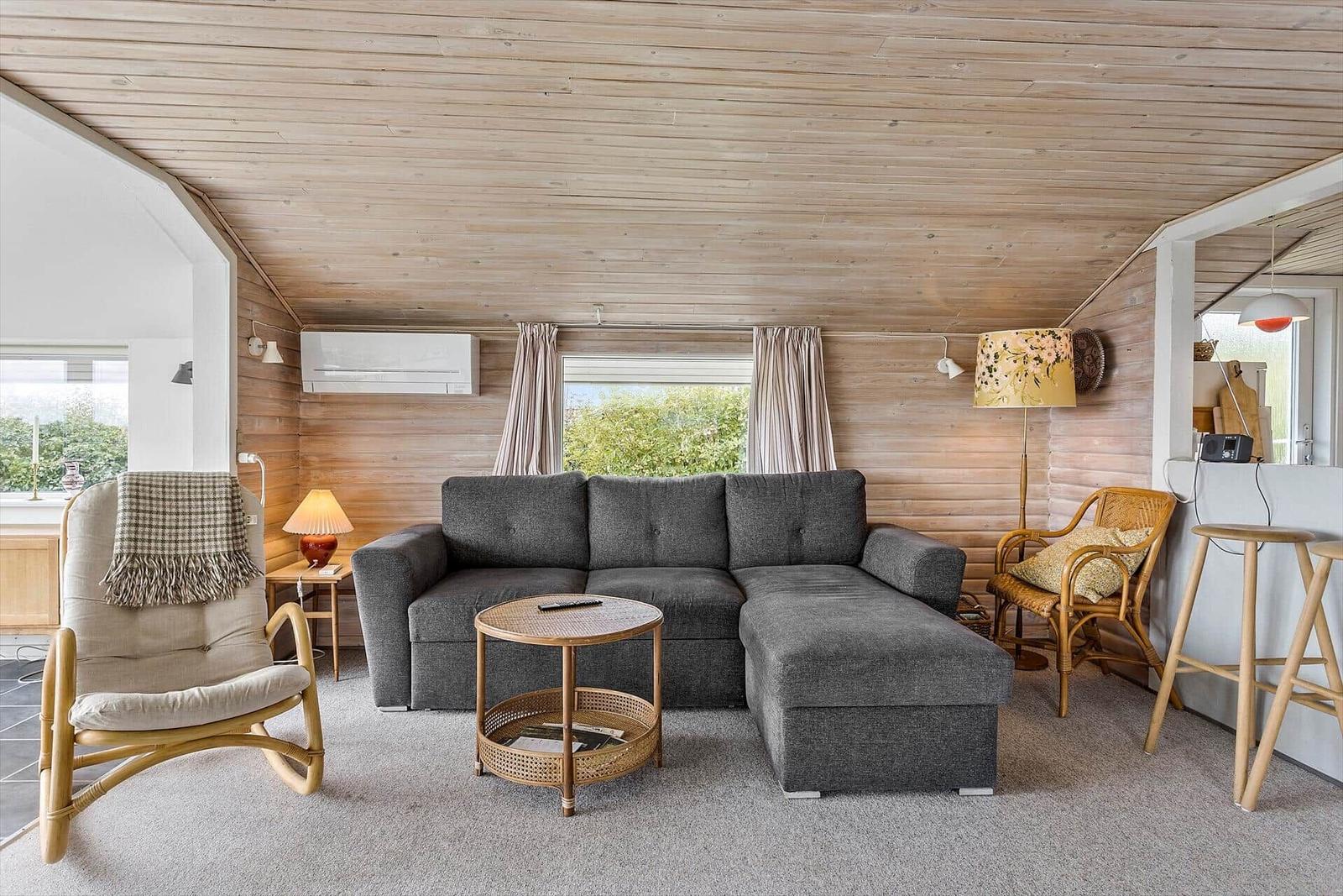 Wohnzimmer mit grauem Sofa, Rattanmöbeln und Holzwandverkleidung.