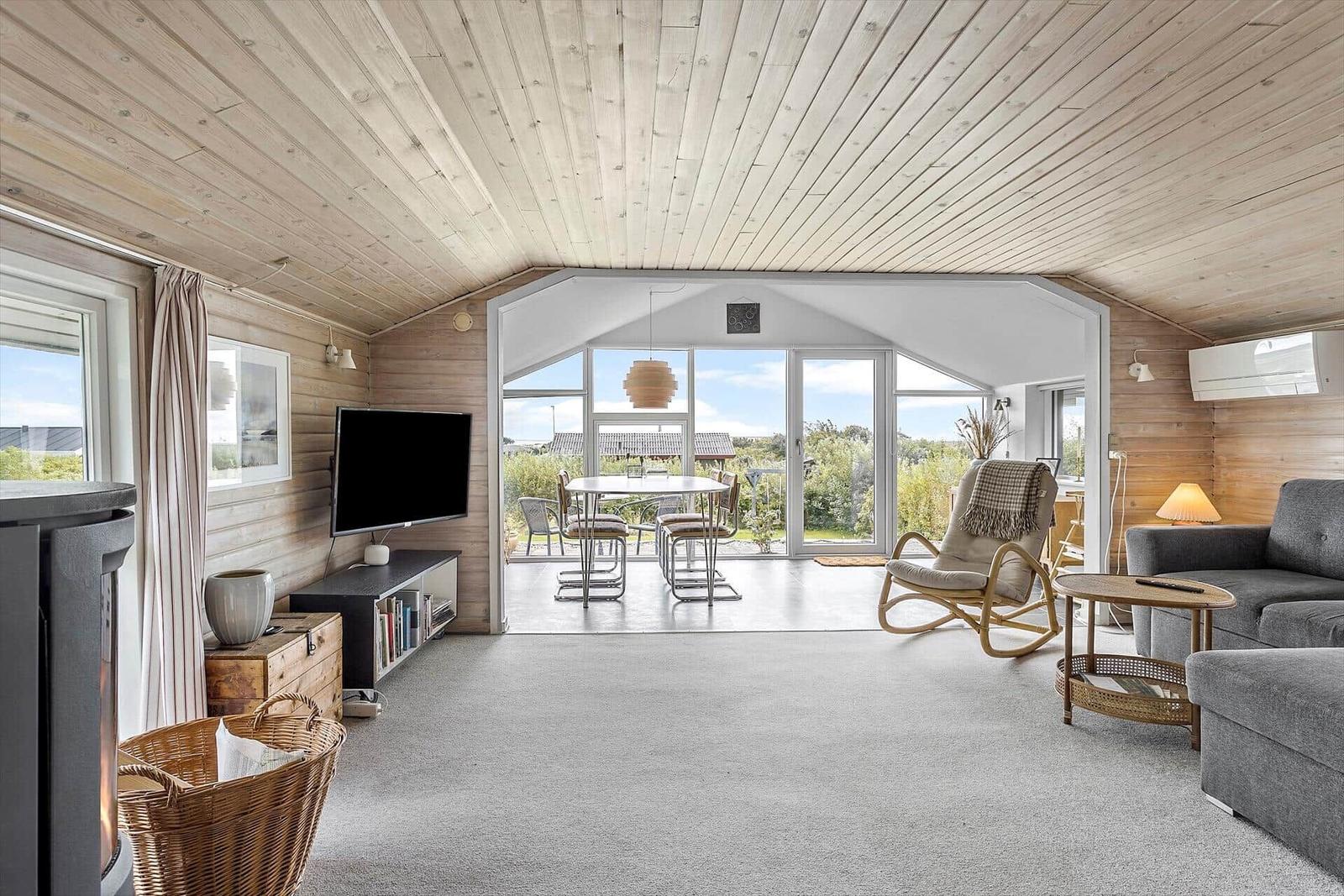 Wohn- und Essbereich mit Holzdecke, Sofa, Schaukelstuhl und Terrasse mit Blick.