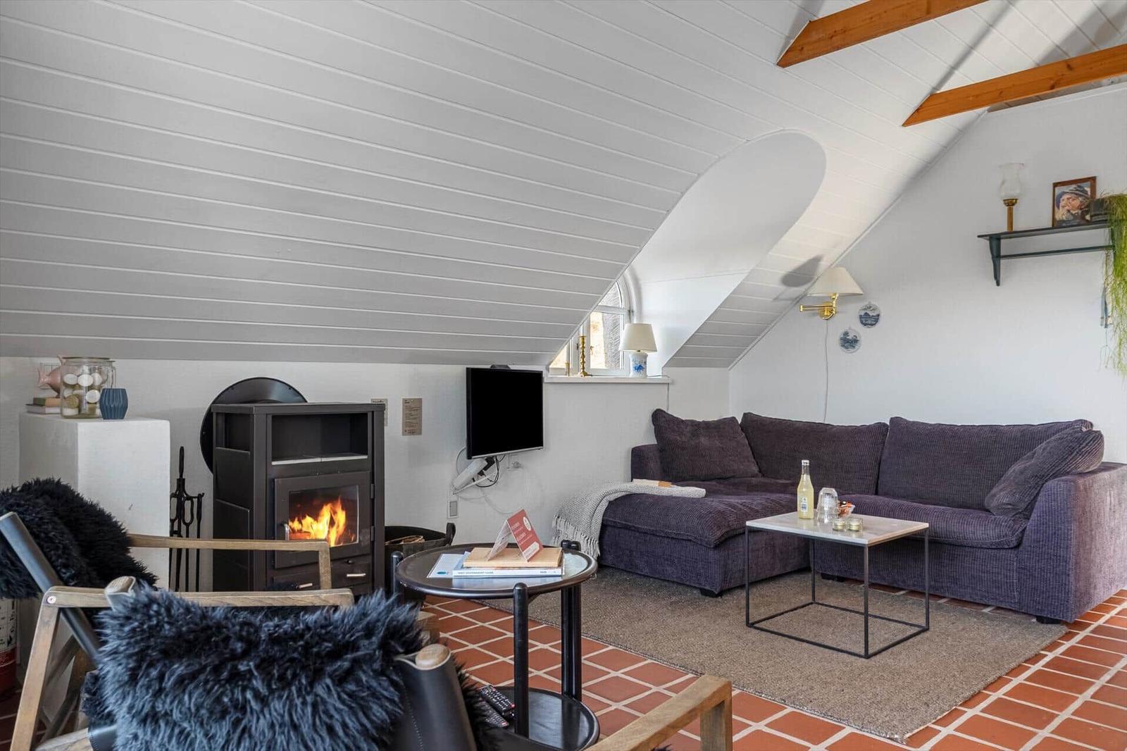 Wohnzimmer mit Kamin, Sofa und TV unter schrägem Dach