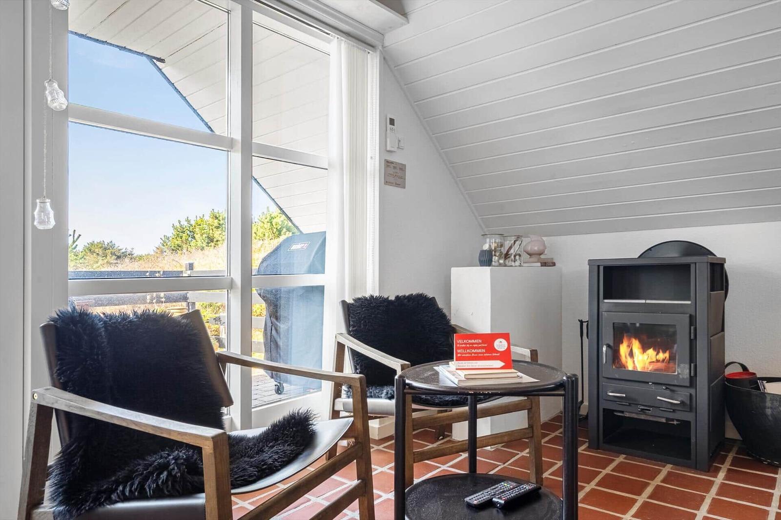 Zwei Sessel mit Fellkissen, Kamin und großes Fenster mit Blick auf Außenbereich.
