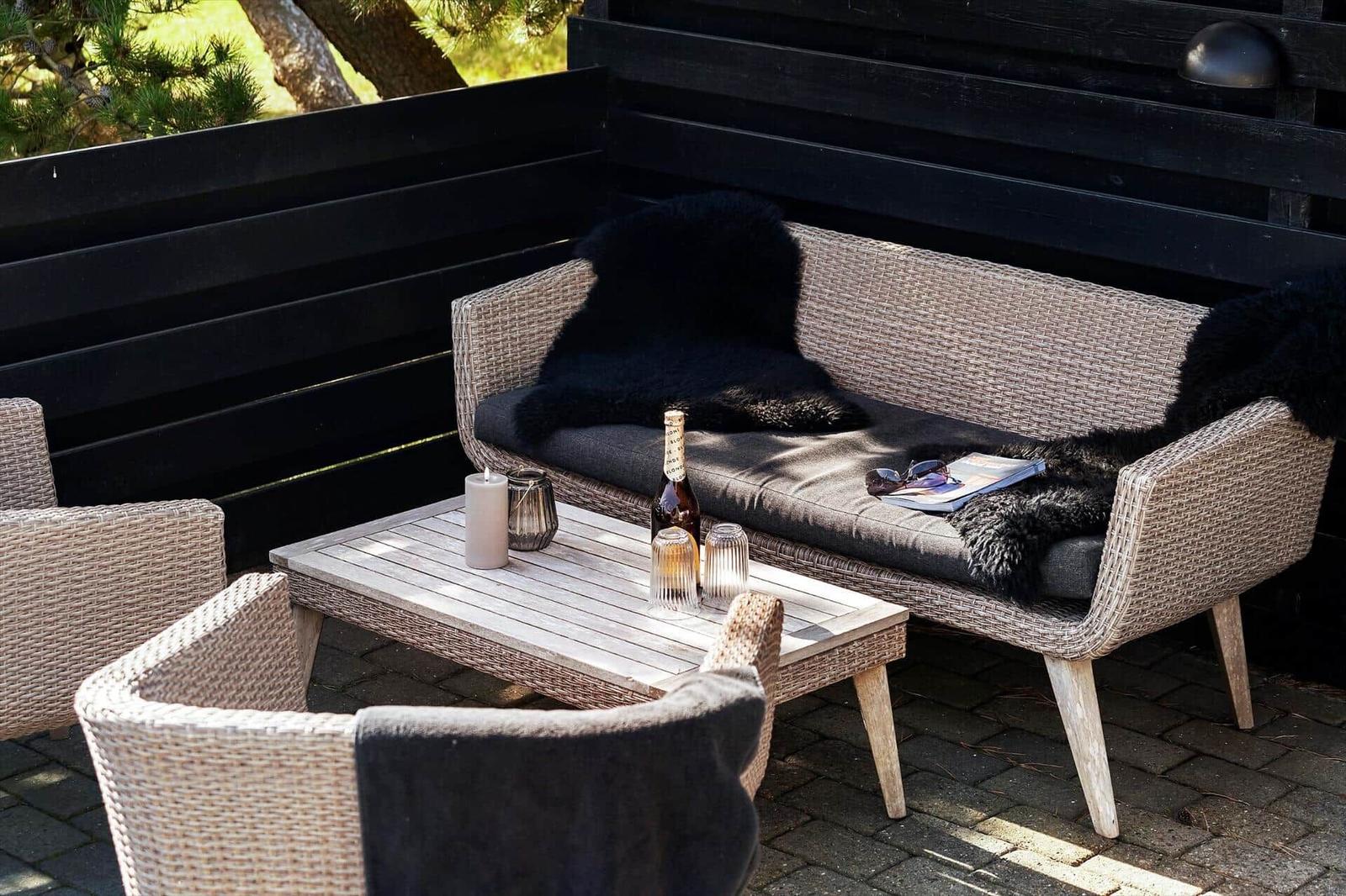 Außenbereich mit wicker Sofa, Tisch und Stühlen. Schwarze Decken und Getränke darauf.