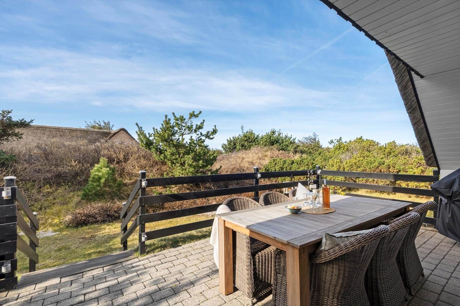 Terrasse mit Tisch und Stühlen, Blick auf Grünflächen und Himmel.