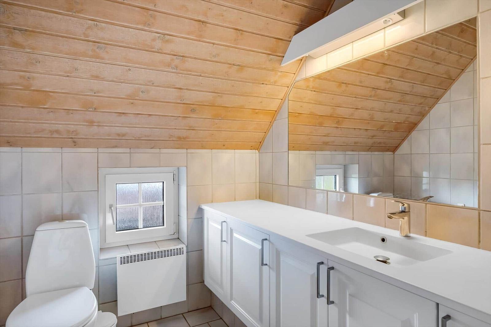 Badezimmer mit Holzdecke, Waschbecken, Spiegel und Toilette.