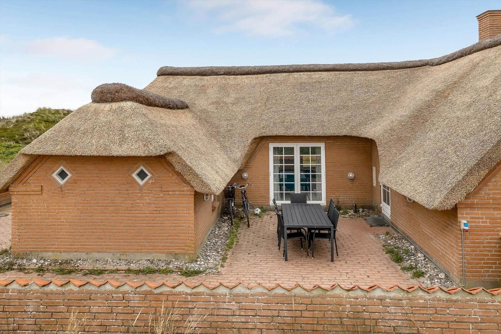 Haus mit Strohdach, Terrasse mit Tisch und Stühlen, Fahrräder und Backsteinmauer