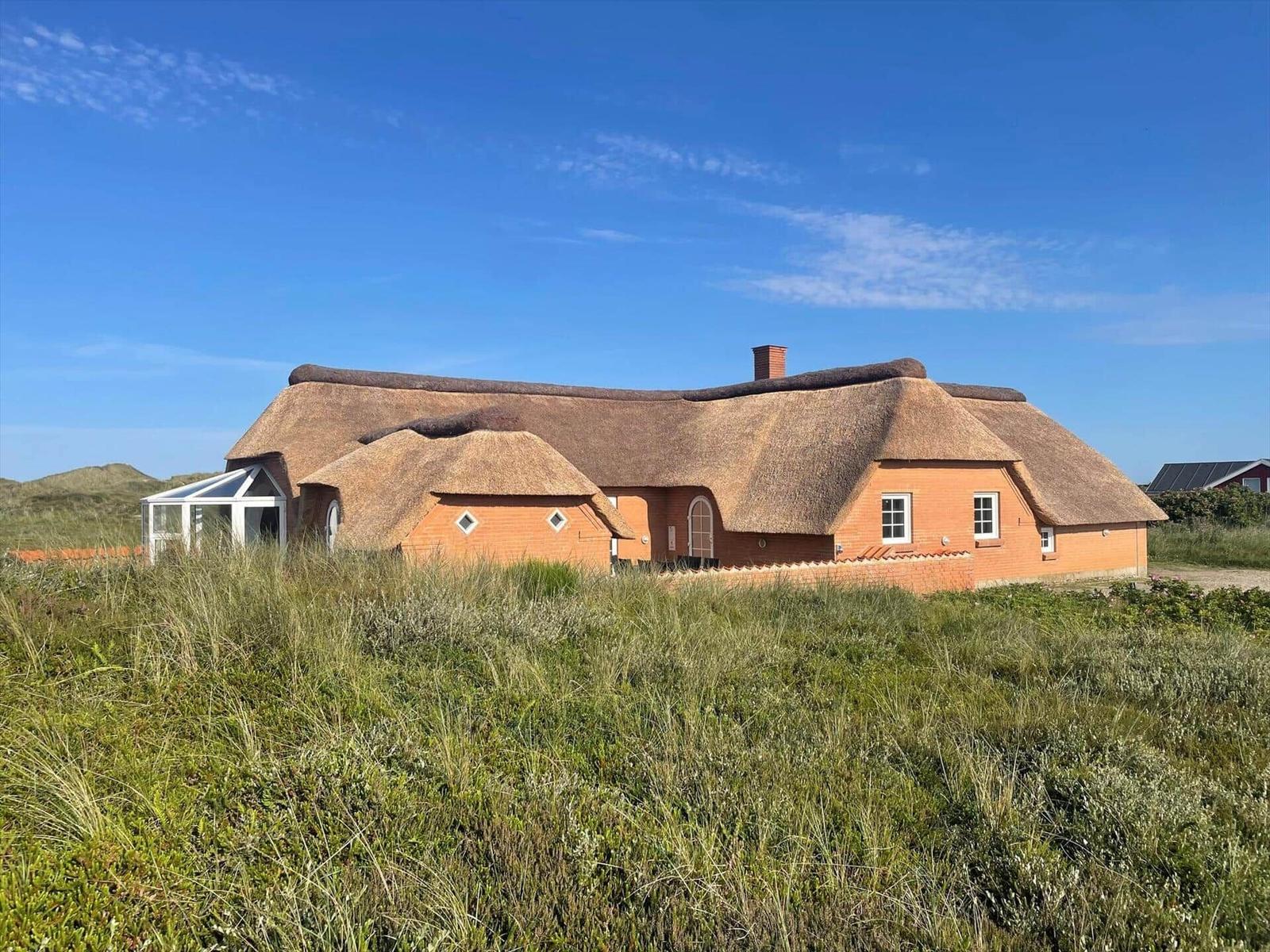Haus mit Strohdach und orangefarbenen Wänden in Grasland unter blauem Himmel.