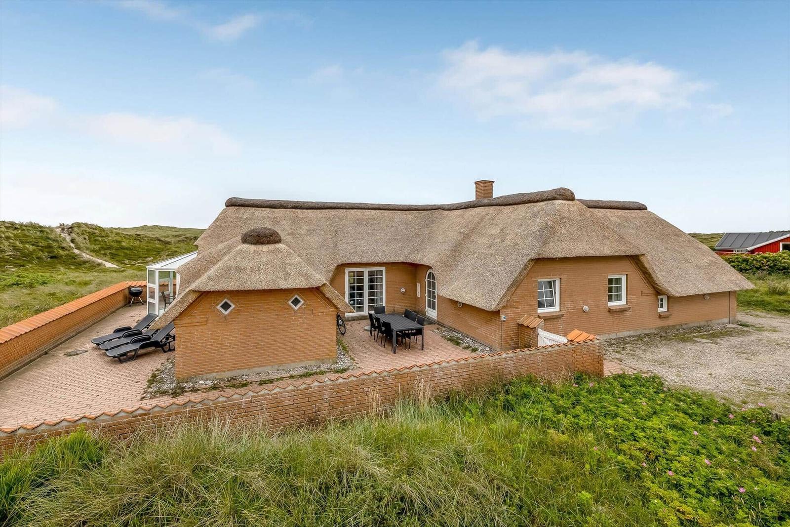 Haus mit Strohdach, Terrasse und Garten. Grill und Liegestühle sind vorhanden.