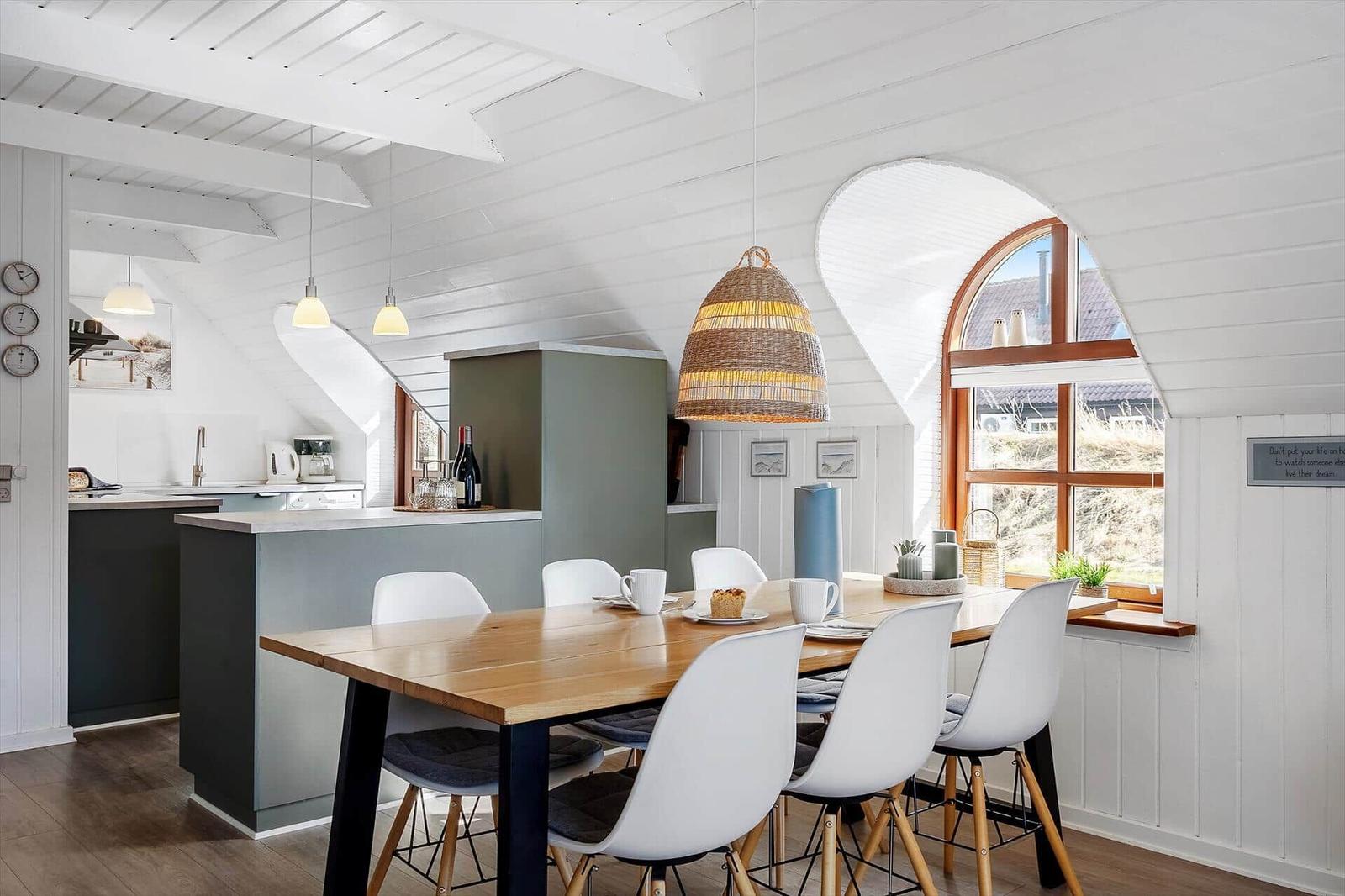Essbereich mit Holztisch und weißen Stühlen unter einem Bambusleuchter. Arches Fenster und weiße Wände.