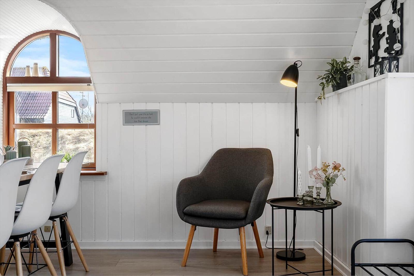 Ein Raum mit grauer Sitzgelegenheit, Tisch und Lampe. Fenster mit Blick auf Außenbereich.