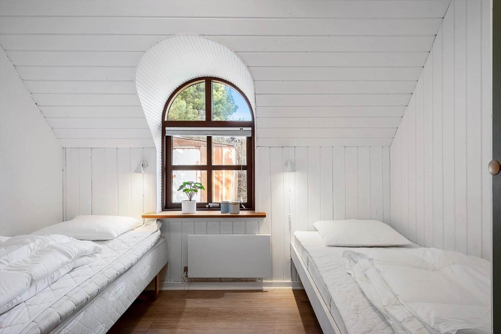 Zwei Betten unter einem Bogenfenster in einem hellen Raum mit Holzboden und weißen Wänden.