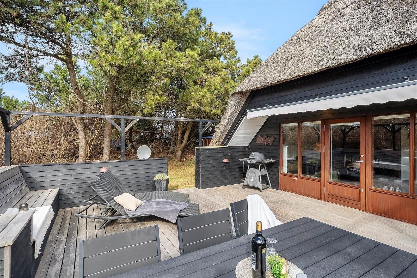 Terrasse mit Grill, Liegen und Tisch unter einem Strohdach.