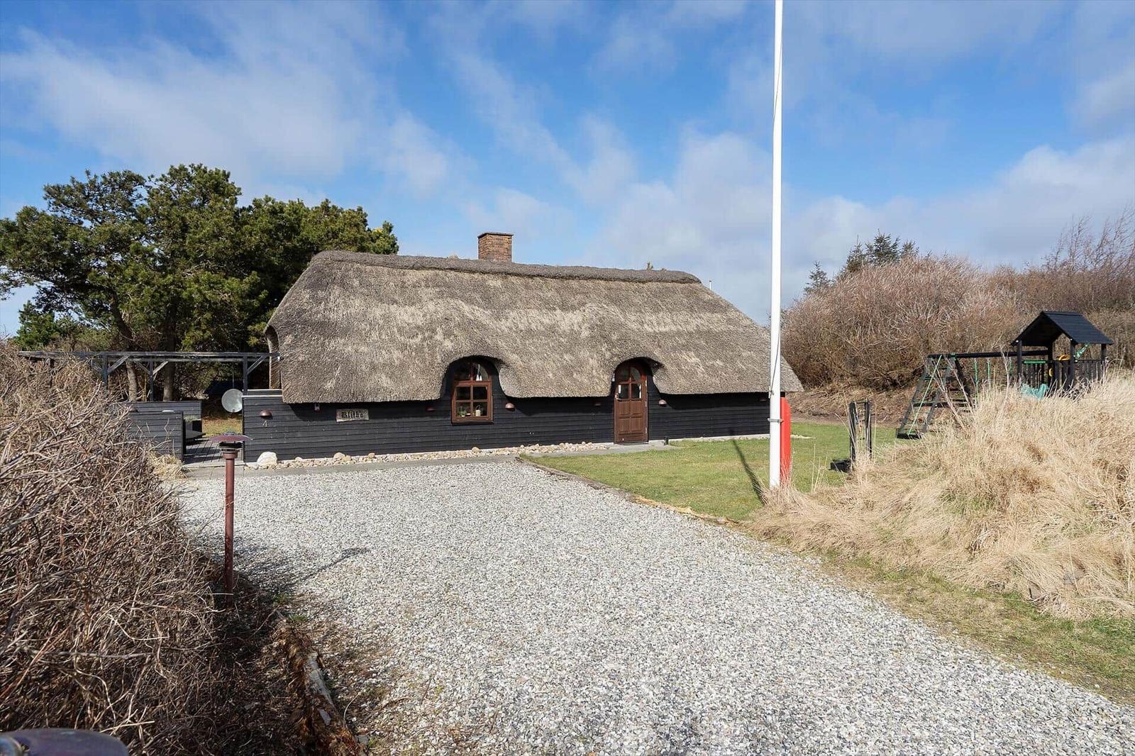 Dorfhaus mit Strohdach, Holztüren und Fenstern. Vor dem Haus liegt ein Kiesweg.