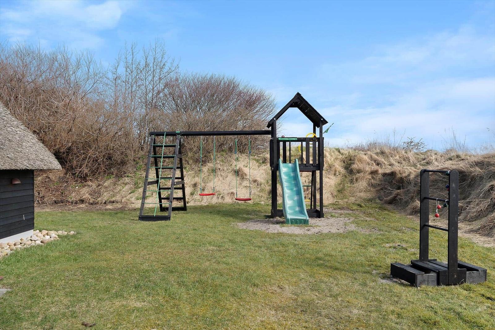 Kinderspielplatz mit Rutsche, Schaukel und Klettergerüst auf grünem Rasen.