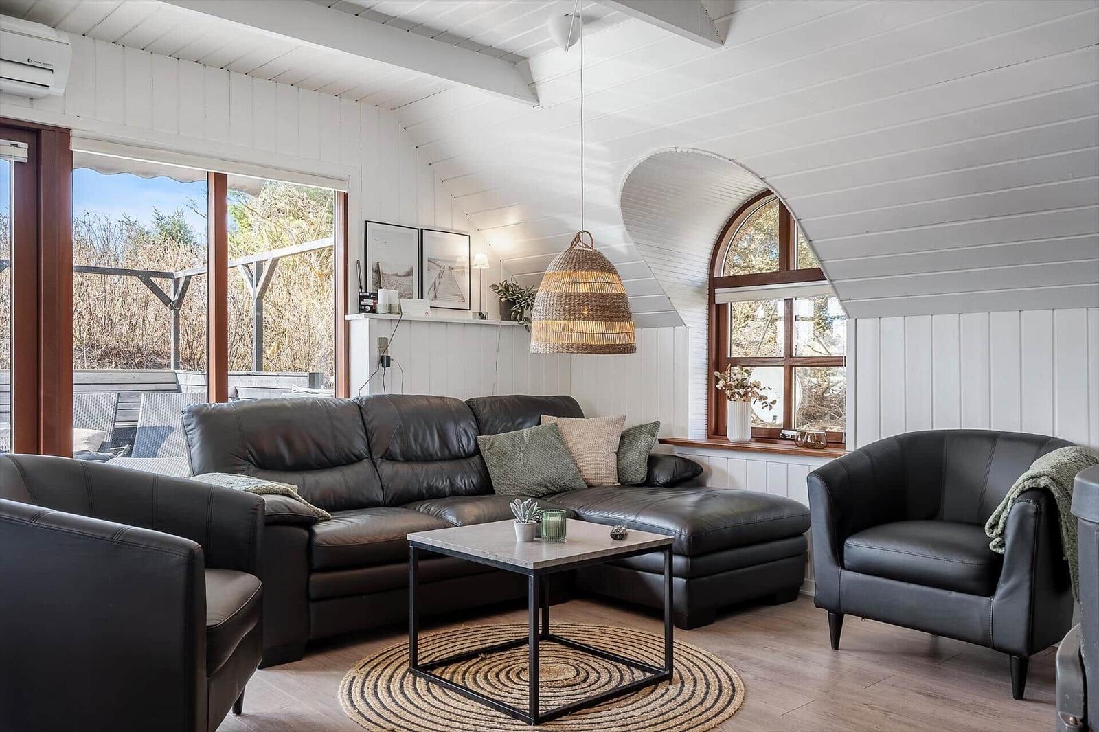 Wohnzimmer mit Ledersofa, Sessel und Holzboden. Große Fenster und helle Wände.