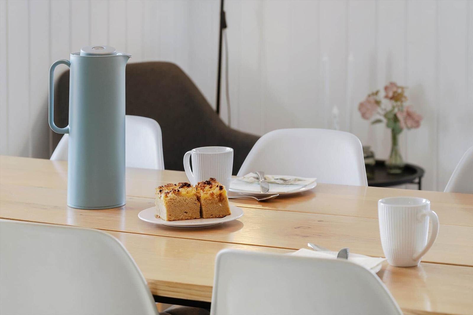 Holztisch mit Tassen, Kaffeebereiter und Kuchenstück.