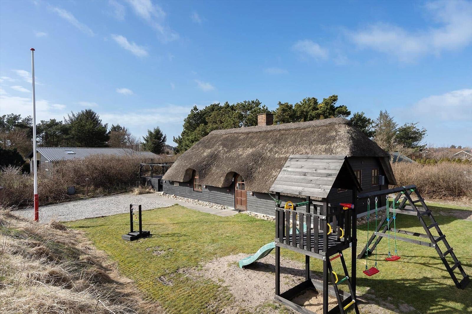 Haus mit Strohdach und Spielplatz im Garten.