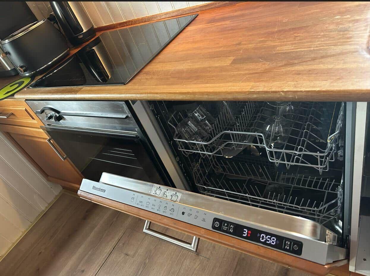 Ein geöffneter Spülmaschinenkasten mit Glas und Besteck. Holzoberfläche und Edelstahlgeräte.