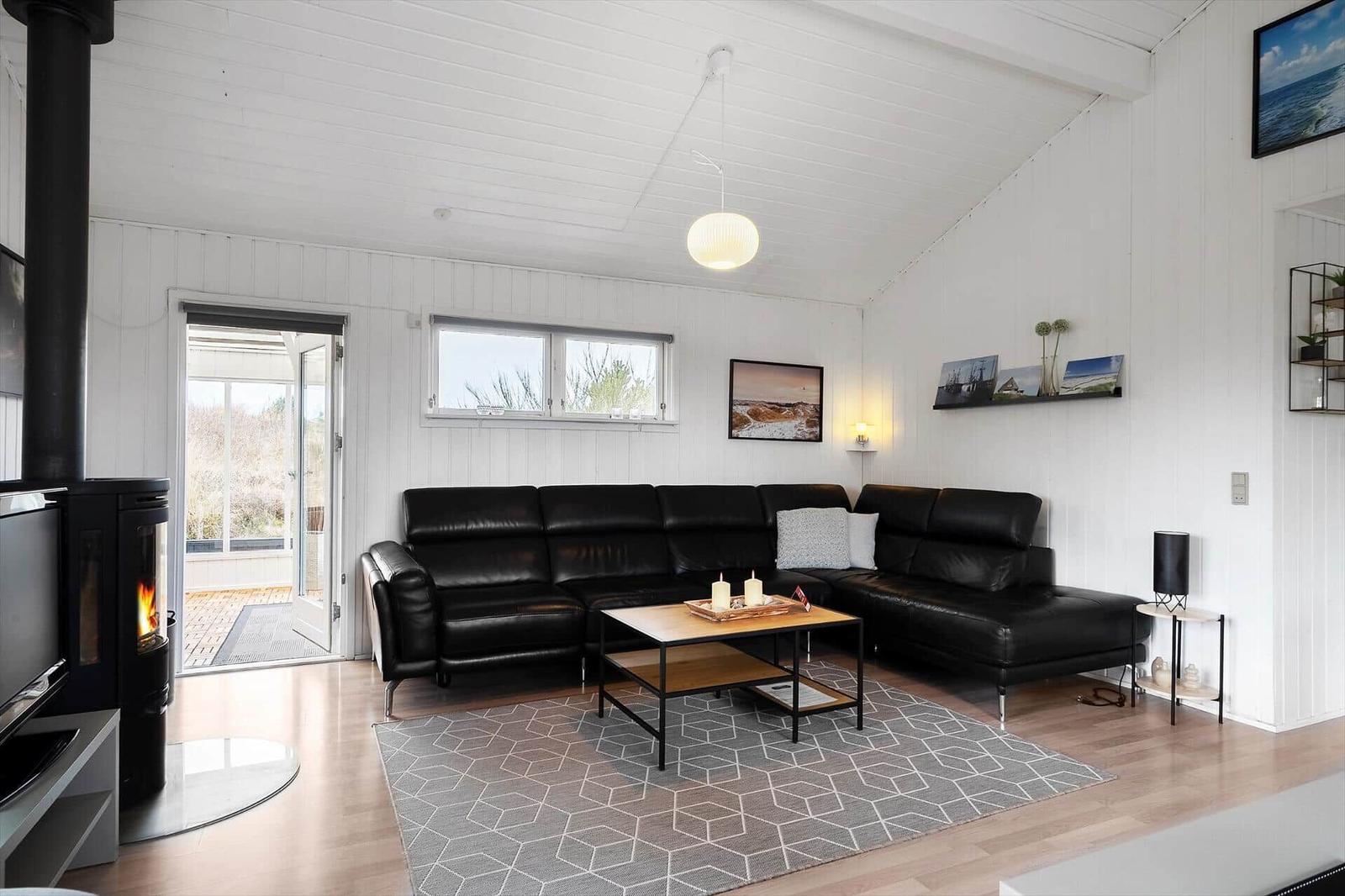 Wohnzimmer mit schwarzer Ledercouch, Holztisch und Kamin. Weiße Wände und Holzboden.