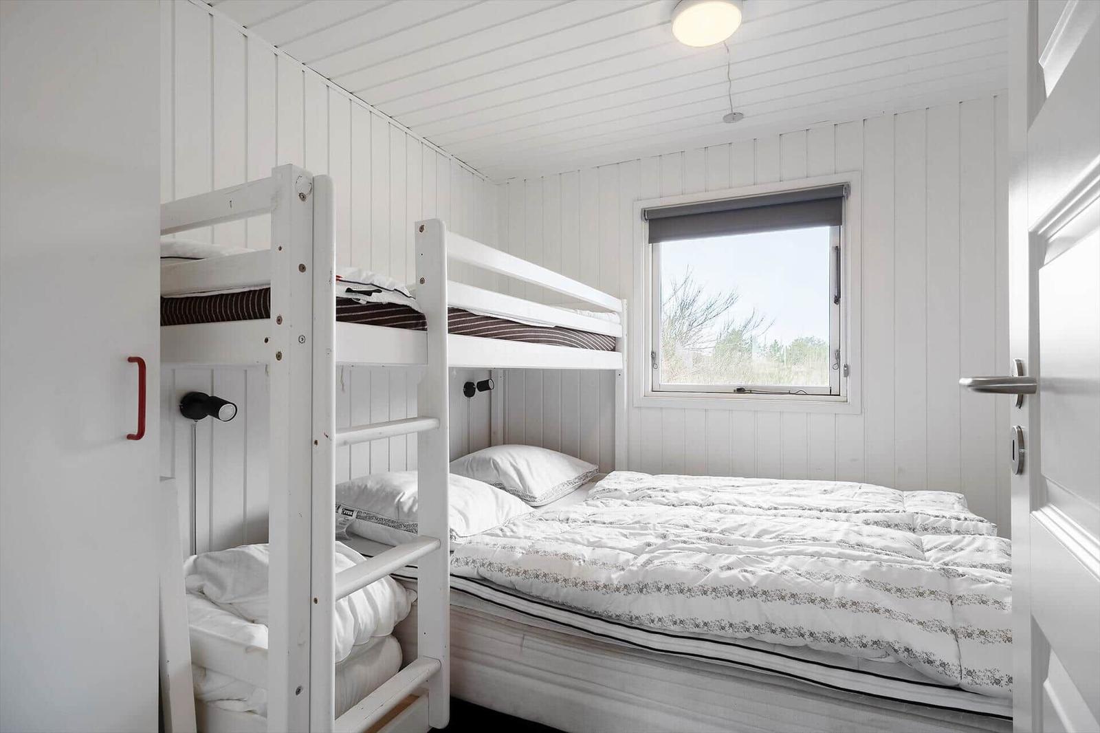 Zimmer mit Doppelbett und Hochbett, weiß verkleidet, Fenster mit Blick nach draußen.