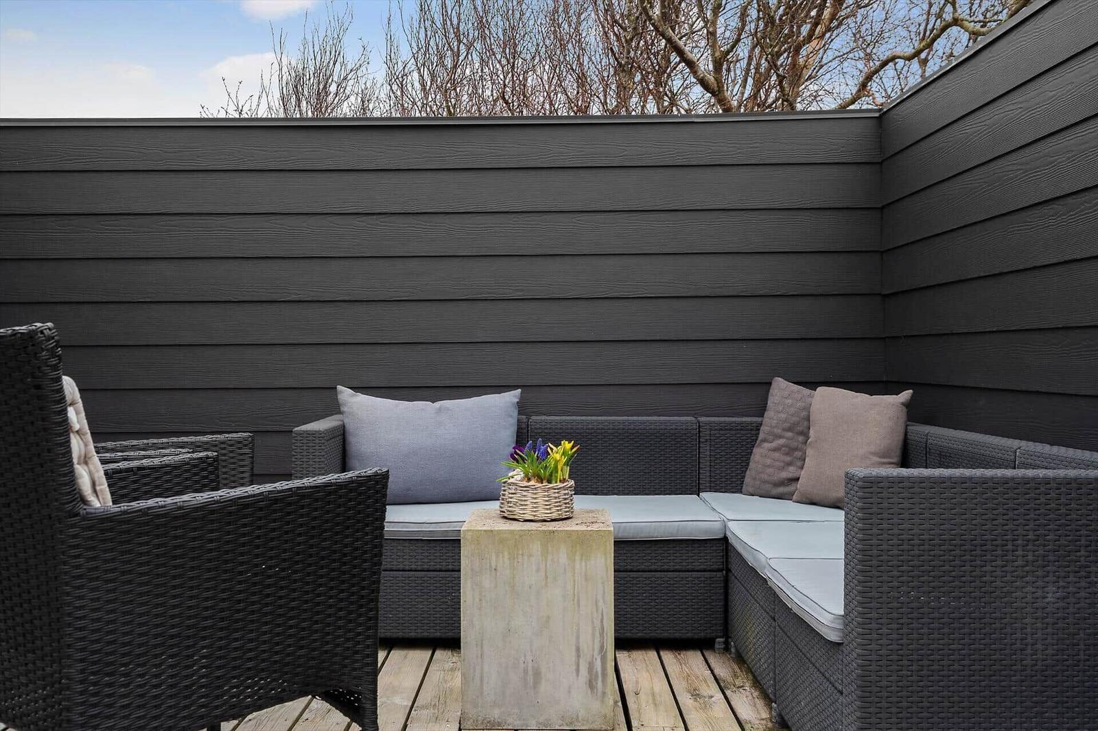 Terrasse mit Sitzgruppe, Pflanzen und Holzboden. Dunkle Holzwände umgeben den Außenbereich.