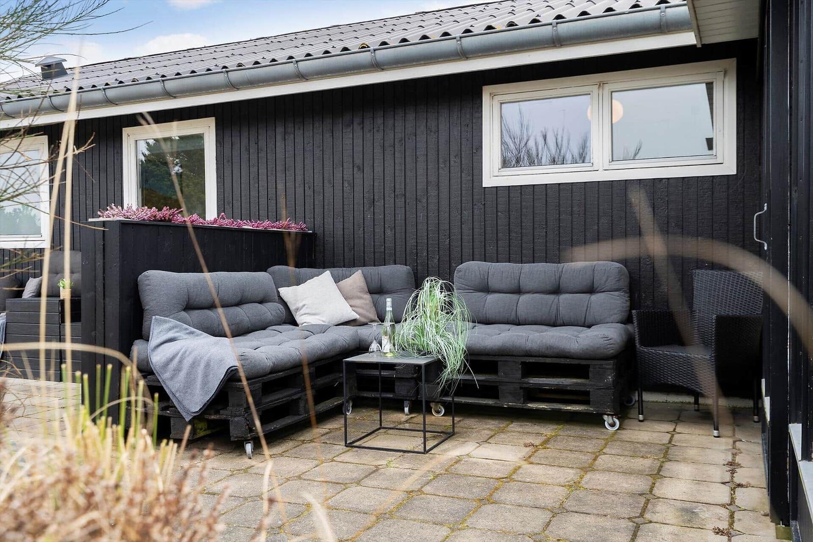 Außenbereich mit grauem Sofa und Tisch vor schwarzem Holzhaus