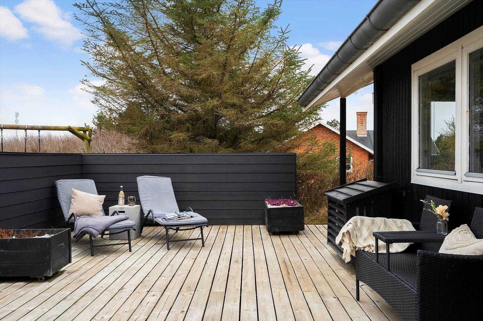 Terrasse mit zwei Liegestühlen, Sitzgruppe und Pflanzenkästen. Hintergrund: großer Baum und Haus.