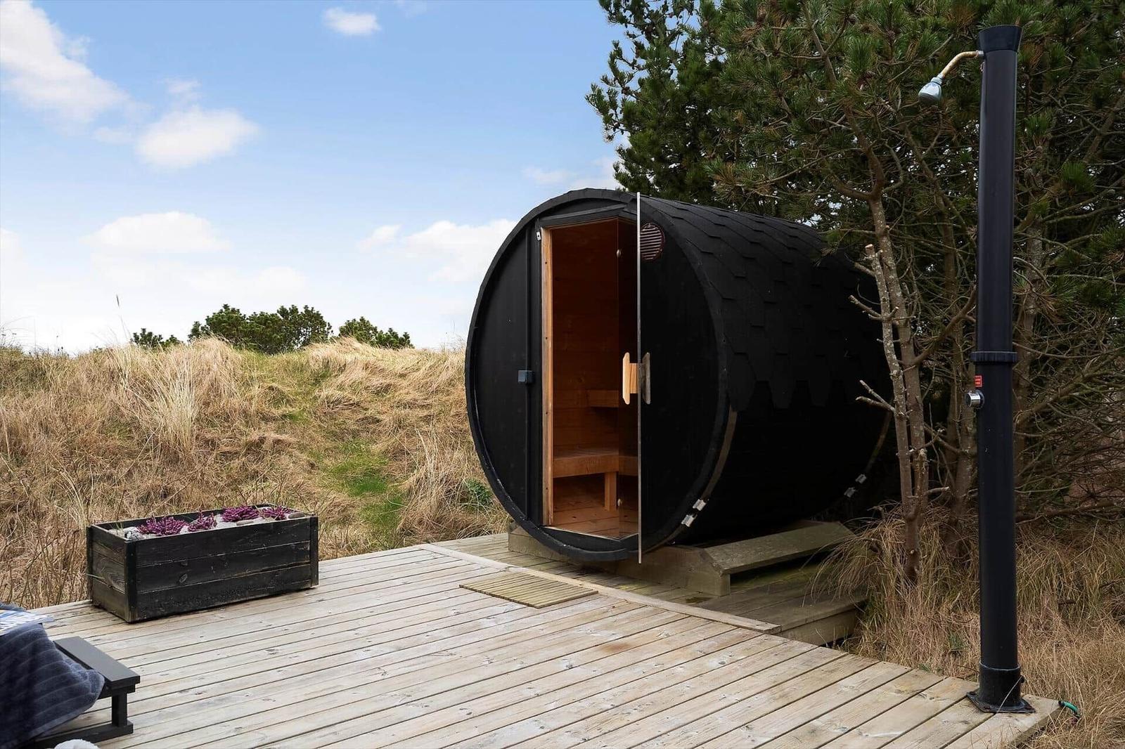 Eine schwarze Sauna auf einer Holzterrasse mit Blick auf Gras und Bäume.