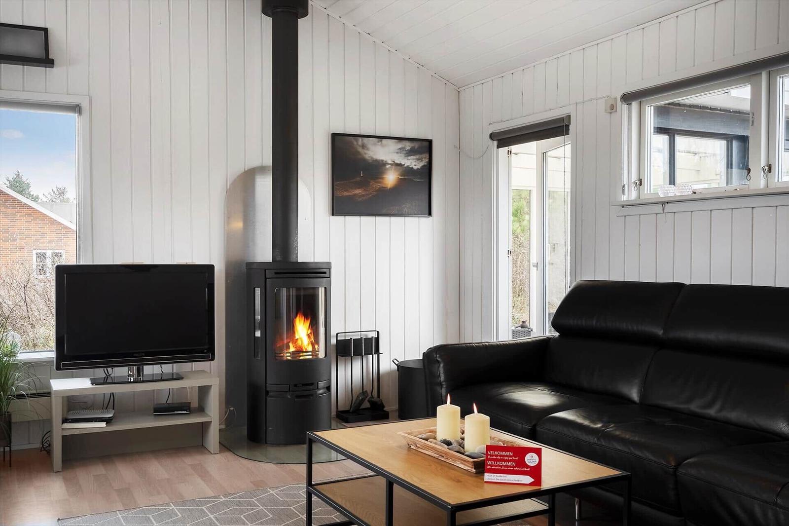 Wohnzimmer mit schwarzer Ledercouch, Kaminofen und Fernseher. Holzfußboden und weiße Wände.