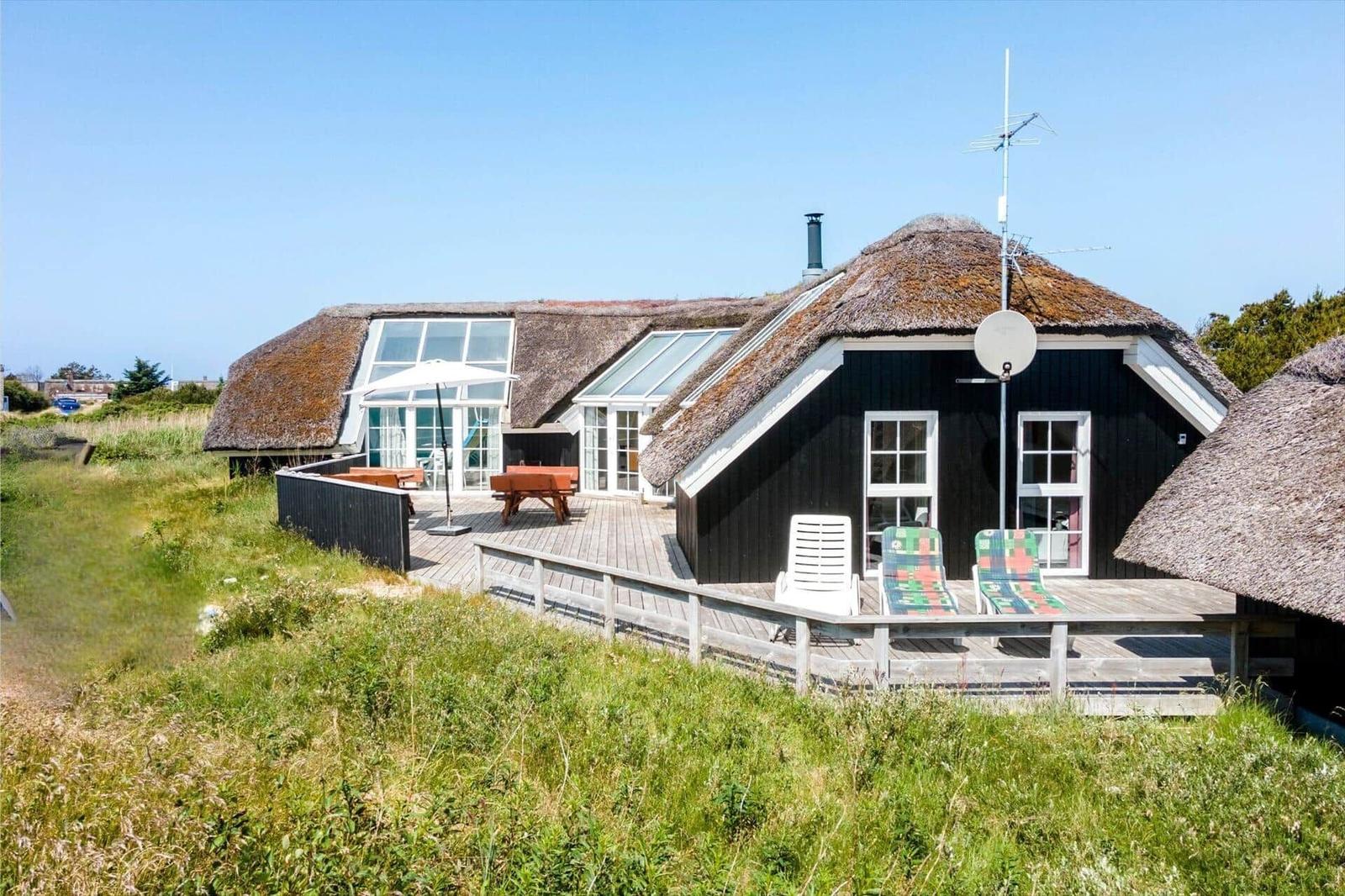 Haus mit Strohdach, Terrasse und Garten. Sonnenschirm, Tische und Liegestühle.
