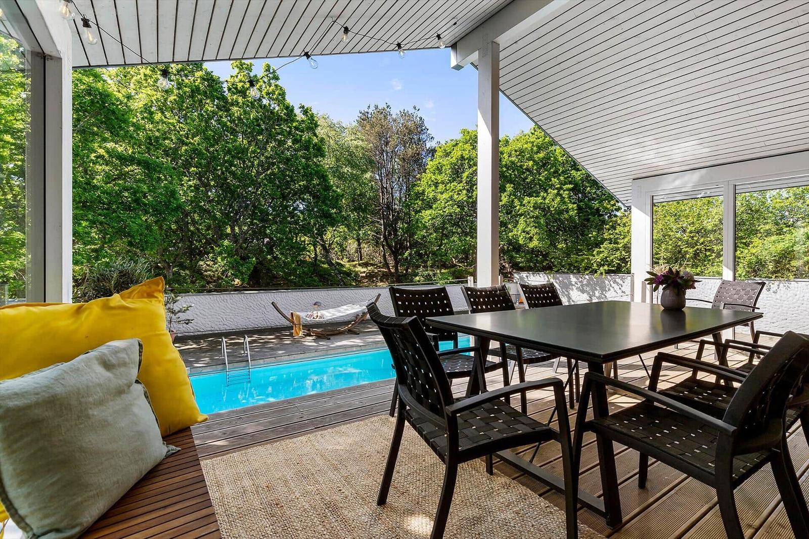Terrasse mit Esstisch, Pool und grüner Umgebung unter weißem Dach.