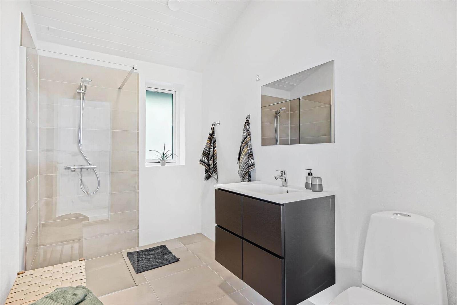 Badezimmer mit Dusche, Waschbecken und Toilette. Fenster mit Pflanze.
