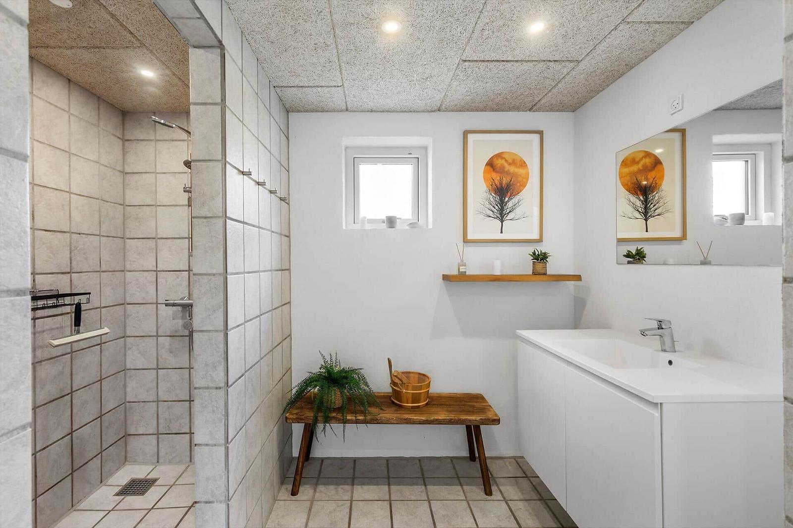 Badezimmer mit Dusche, Waschbecken und Holzbank. Wandbild und Pflanzen.