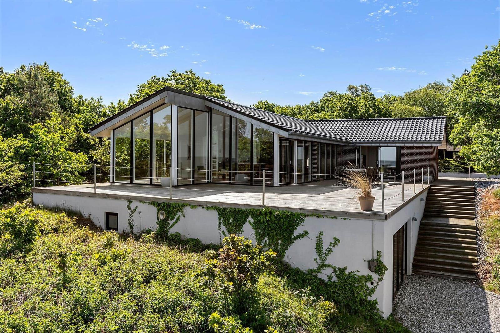 Moderne Villa mit großem Balkon, umgeben von Bäumen und Grünflächen.