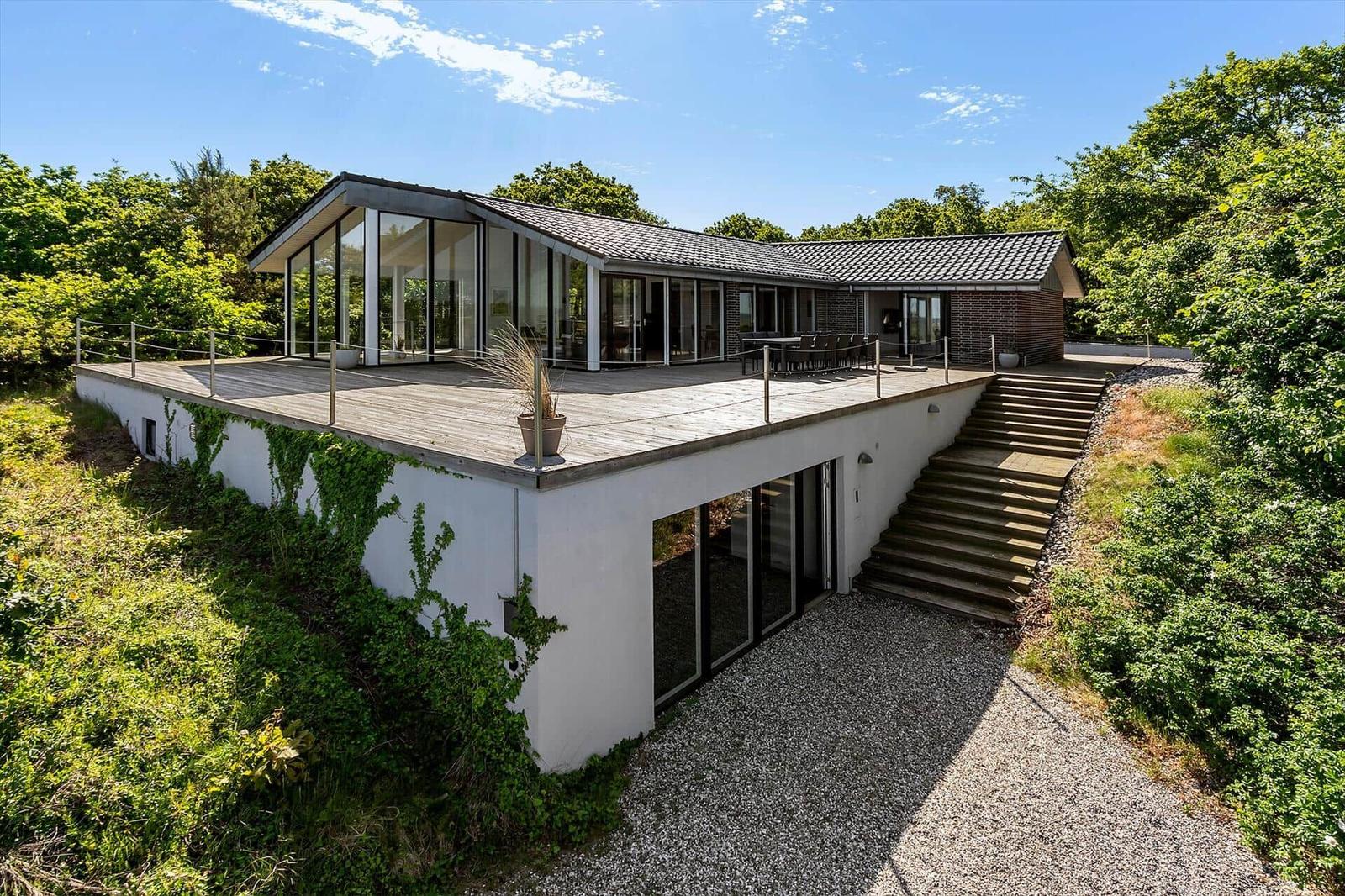 Moderne Villa mit großem Terrassenbereich und Glasfassade in grüner Umgebung.