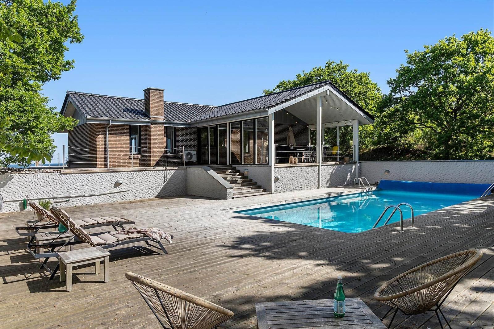 Haus mit Pool, Terrasse und Liegen unter Bäumen.