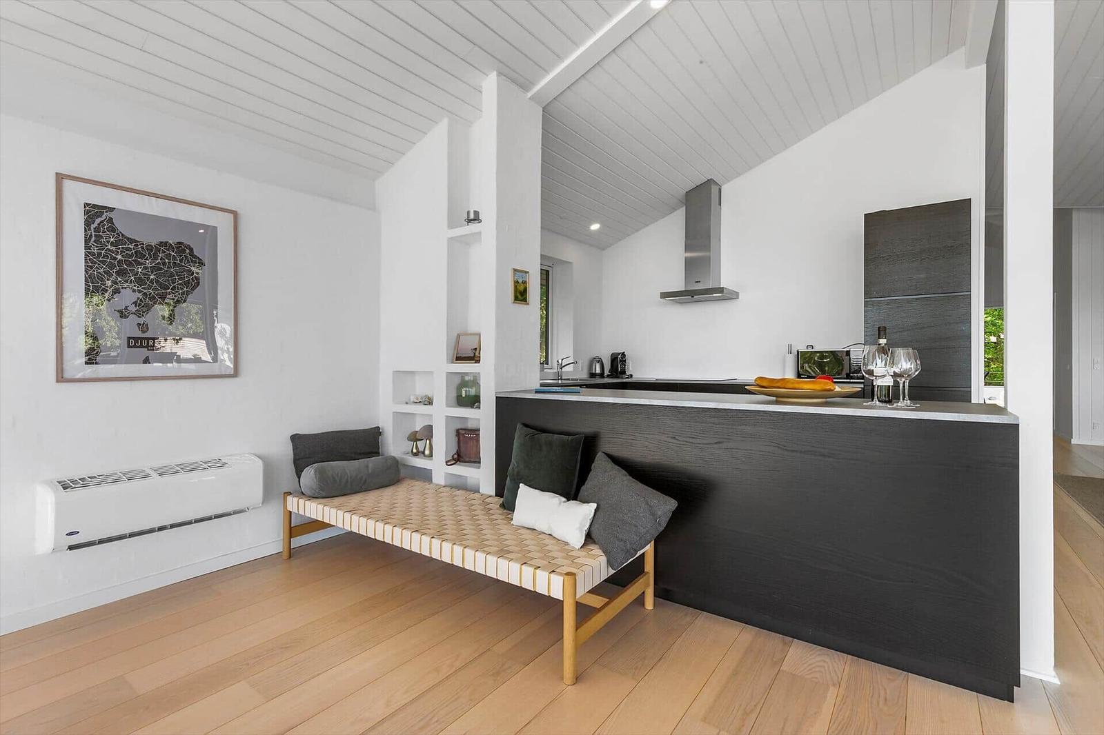 Küche mit dunklem Arbeitsbereich und Sitzbank. Holzboden und weißer Deckenverkleidung.