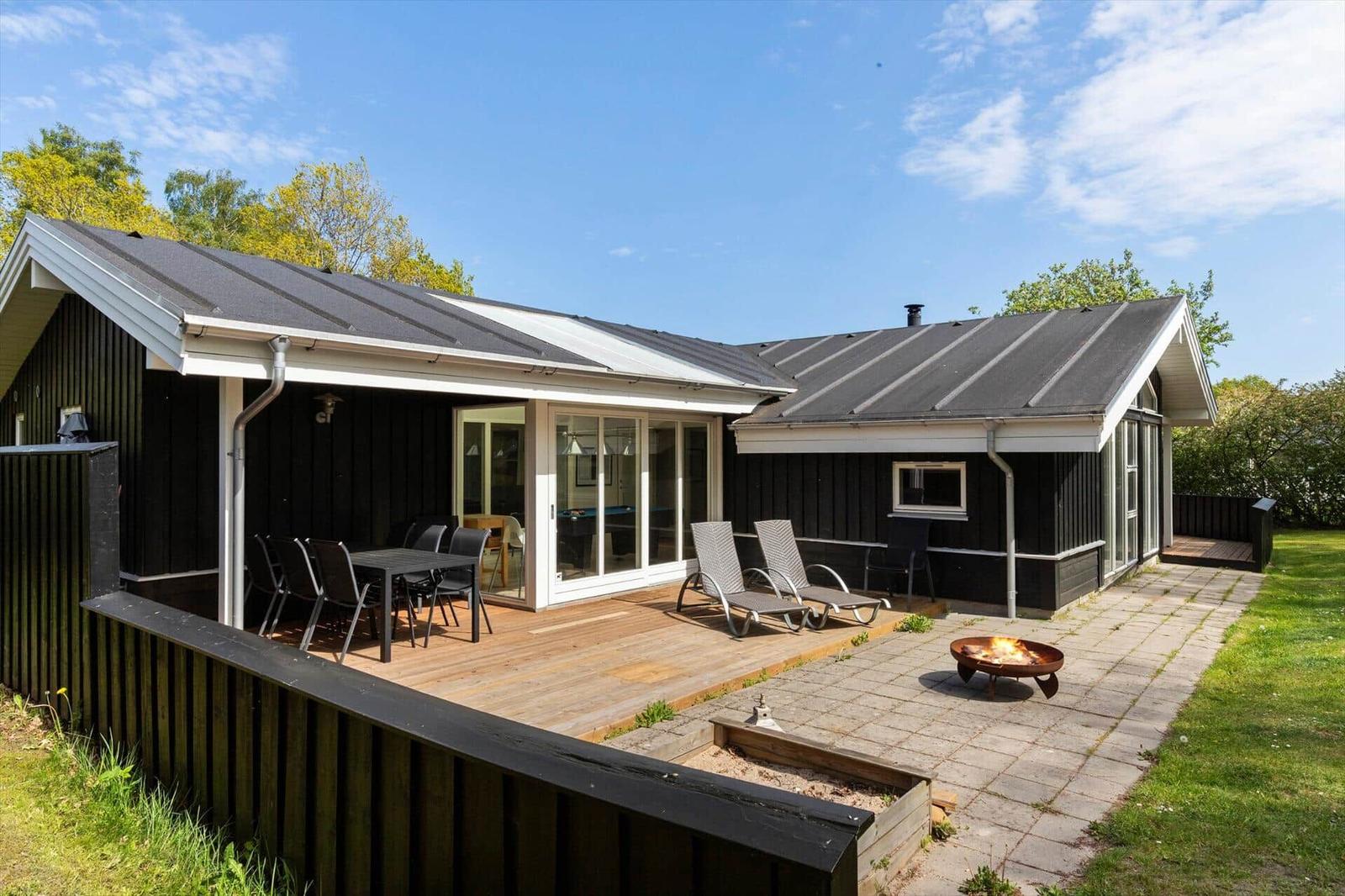 Haus mit Terrasse, Liegestühlen und Feuerkorb. Holzterrasse und Rasenfläche.