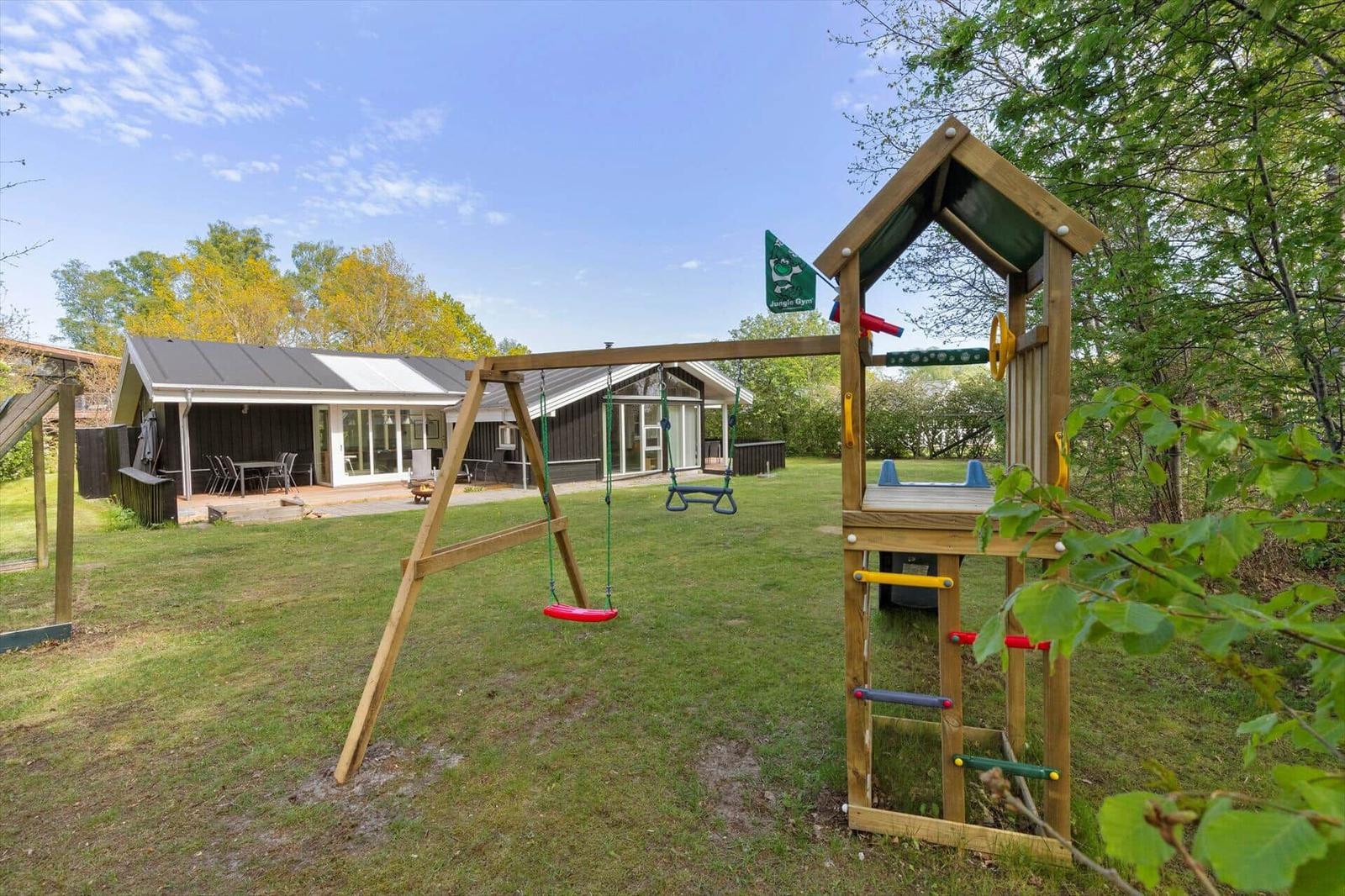 Hinterhof mit Spielplatz, Schaukel und Klettergerüst. Haus mit Terrasse und Sitzgelegenheiten.