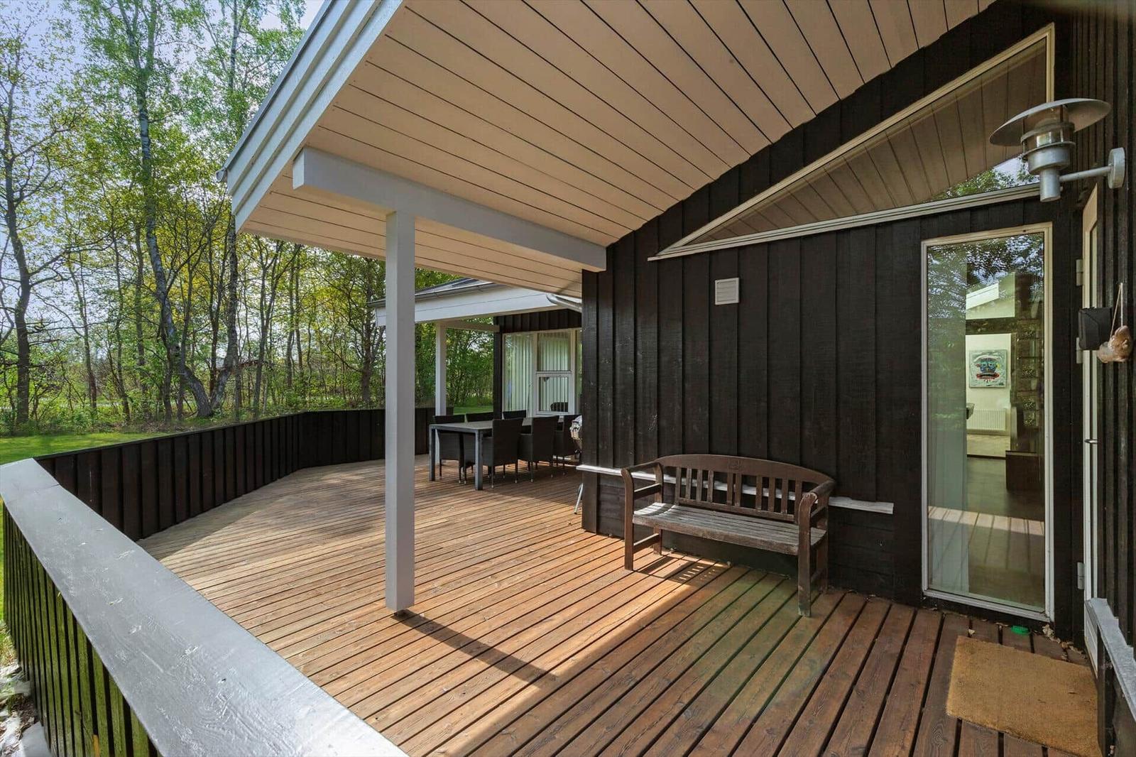 Holzterrasse mit Sitzbank und Tisch unter Dach, Blick in den Wald.