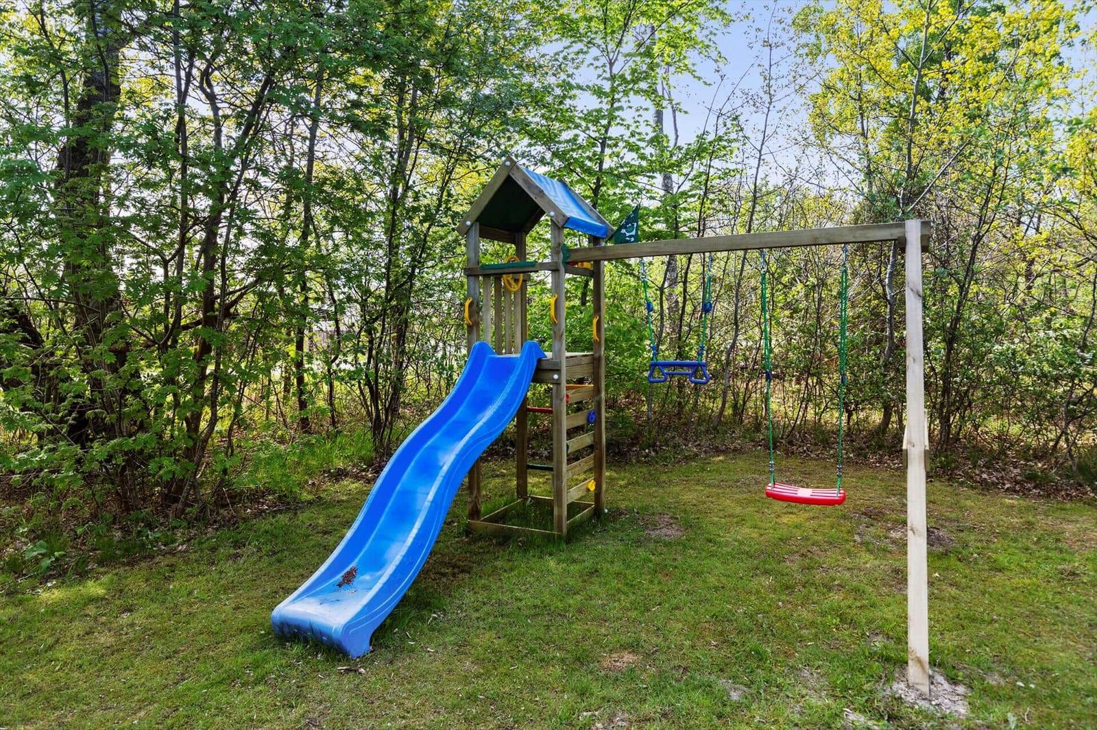 Holzspielplatz mit blauer Rutsche und Schaukel im grünen Garten.