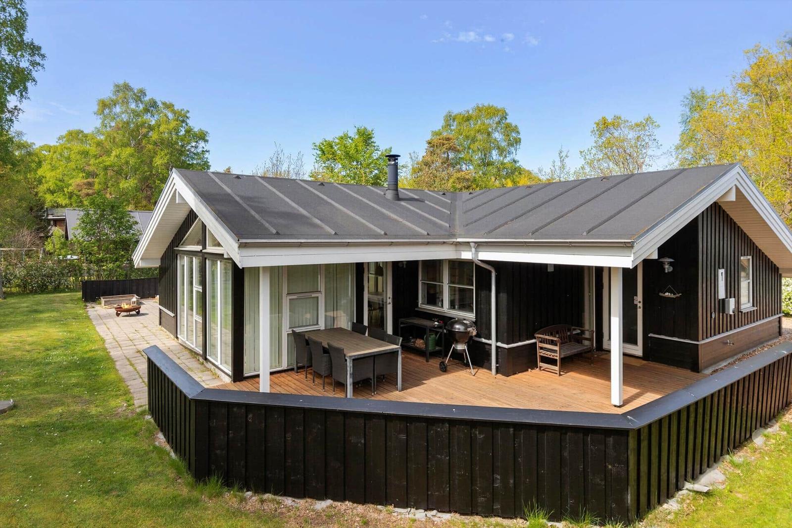 Haus mit Terrasse, Grill und Garten. Holzverkleidung und Dach aus Metall.