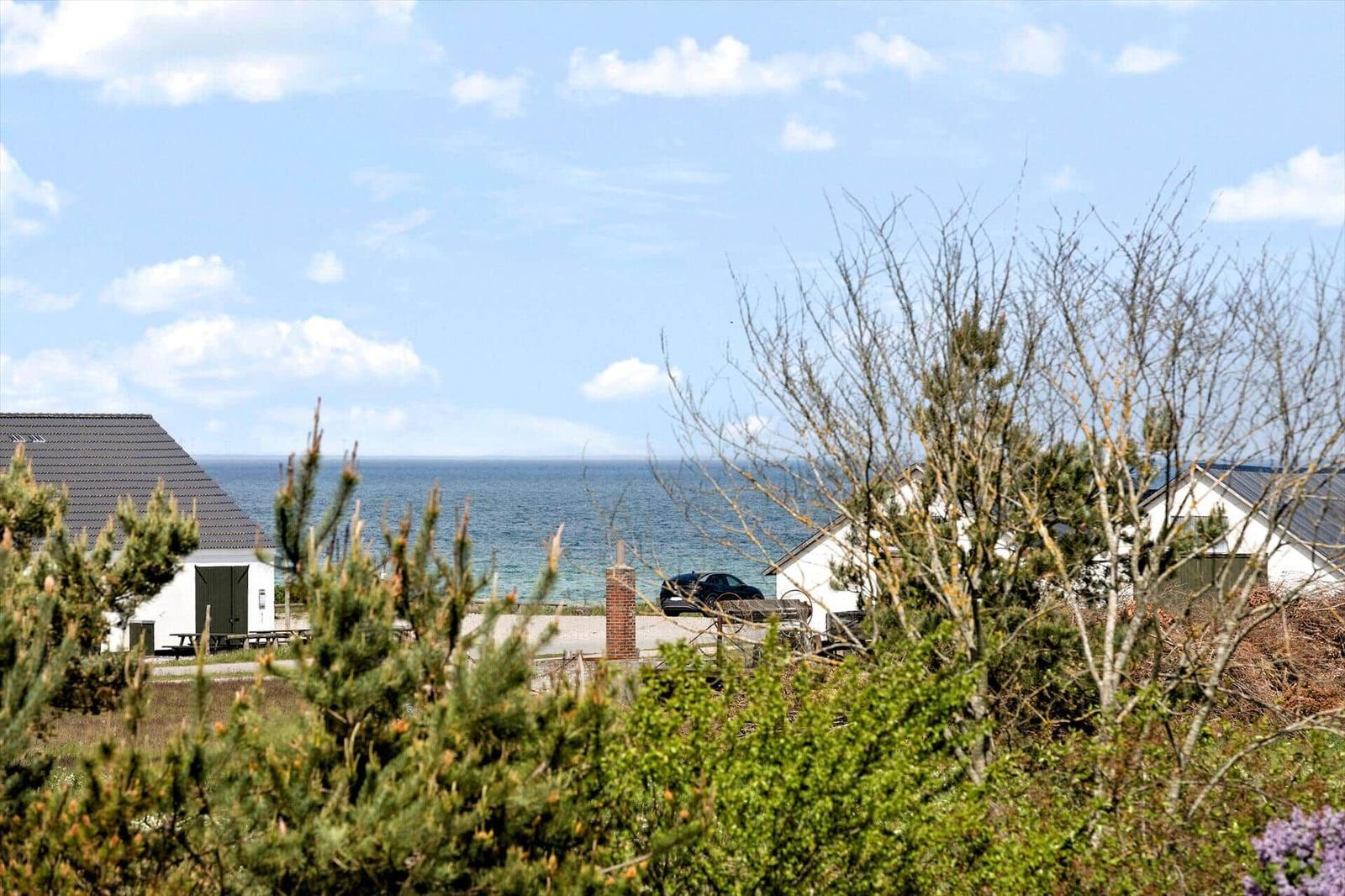 Meerblick von einem Garten mit Bäumen und Häusern. Ein Auto steht auf einem Hof.
