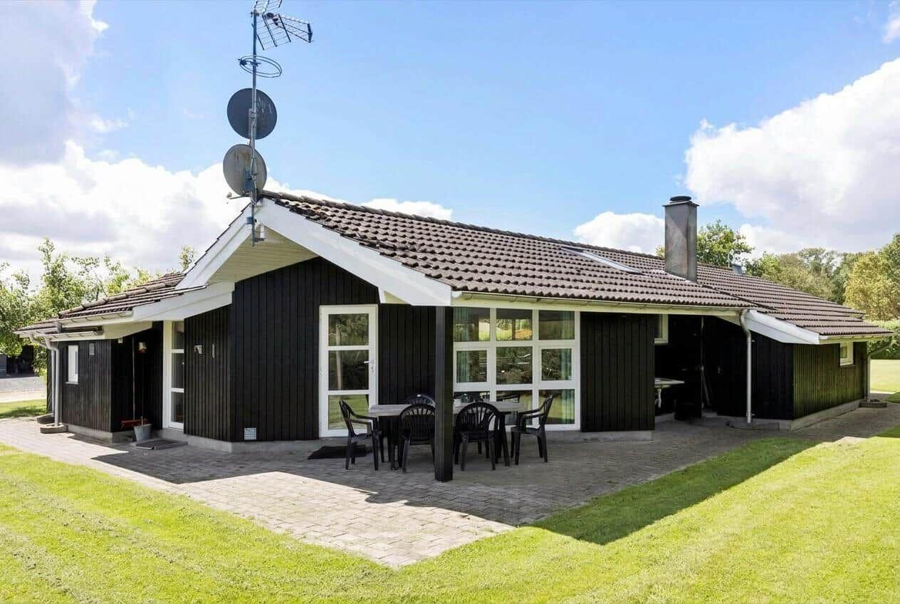 Ein schwarz-weißes Haus mit Terrasse und Garten. Satellitenschüssel und Schornstein sind sichtbar.