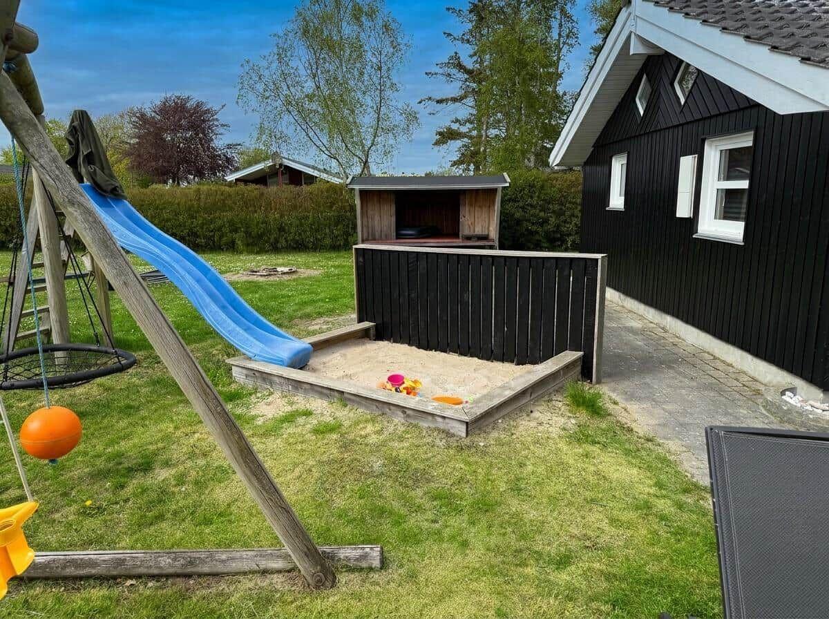 Hinterhof mit Sandkasten, Rutsche und Spielgerät. Schwarzes Haus mit weißen Fenstern.